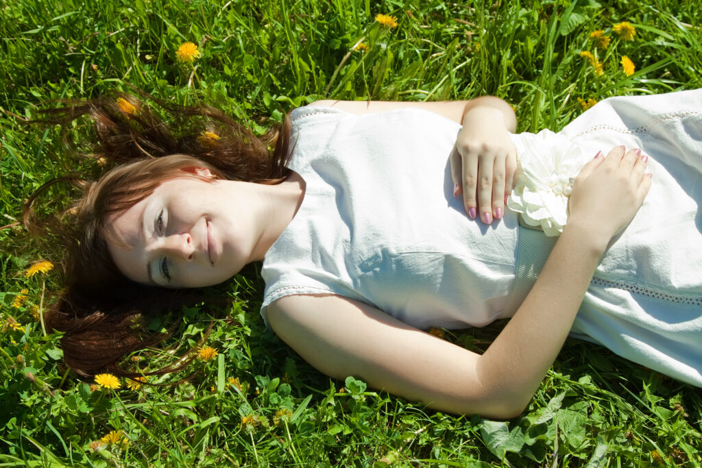 Écouter son corps : femme allongée dans l’herbe, les mains posées sur son ventre.