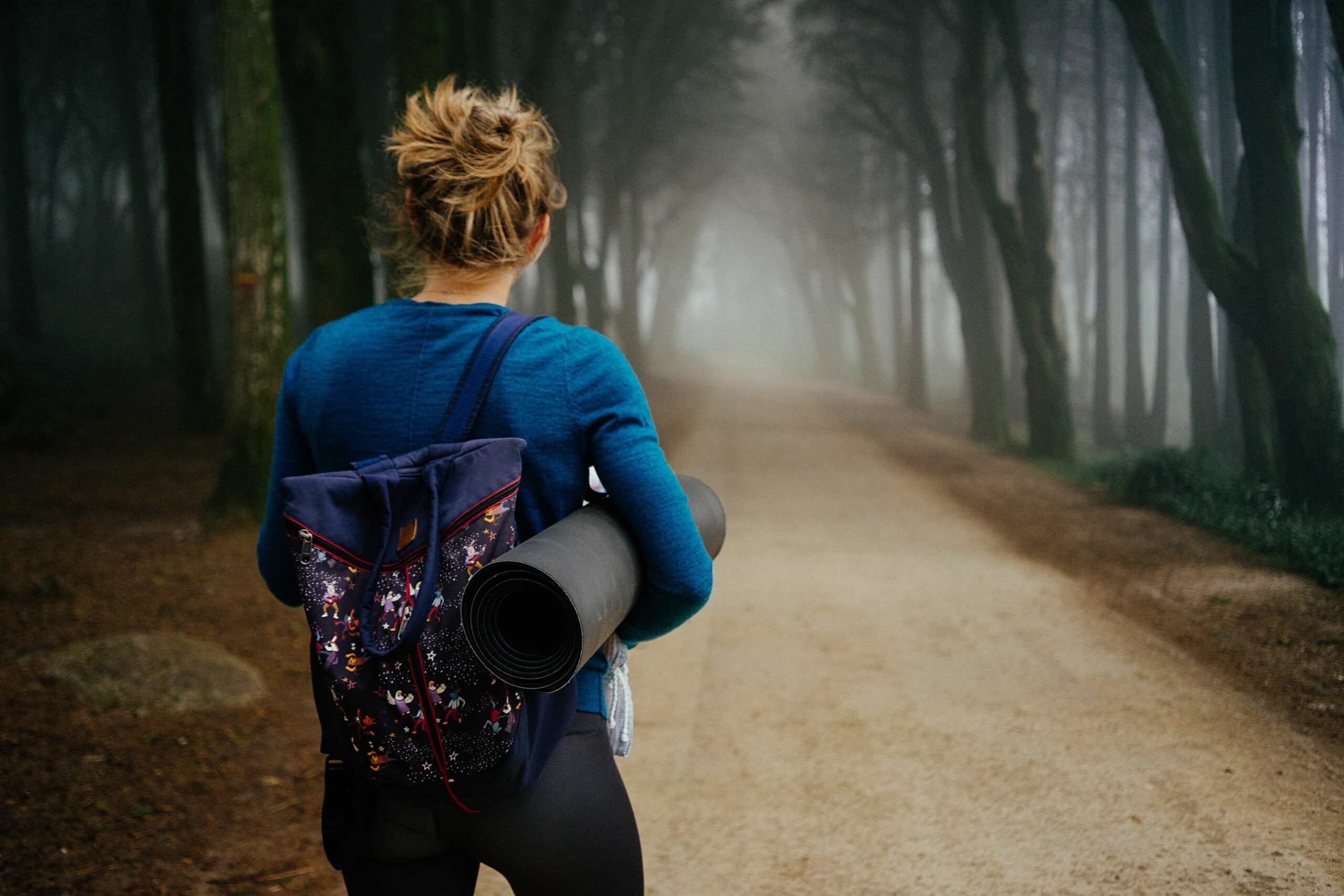Femme marchant en forêt avec un tapis de yoga sous le bras.